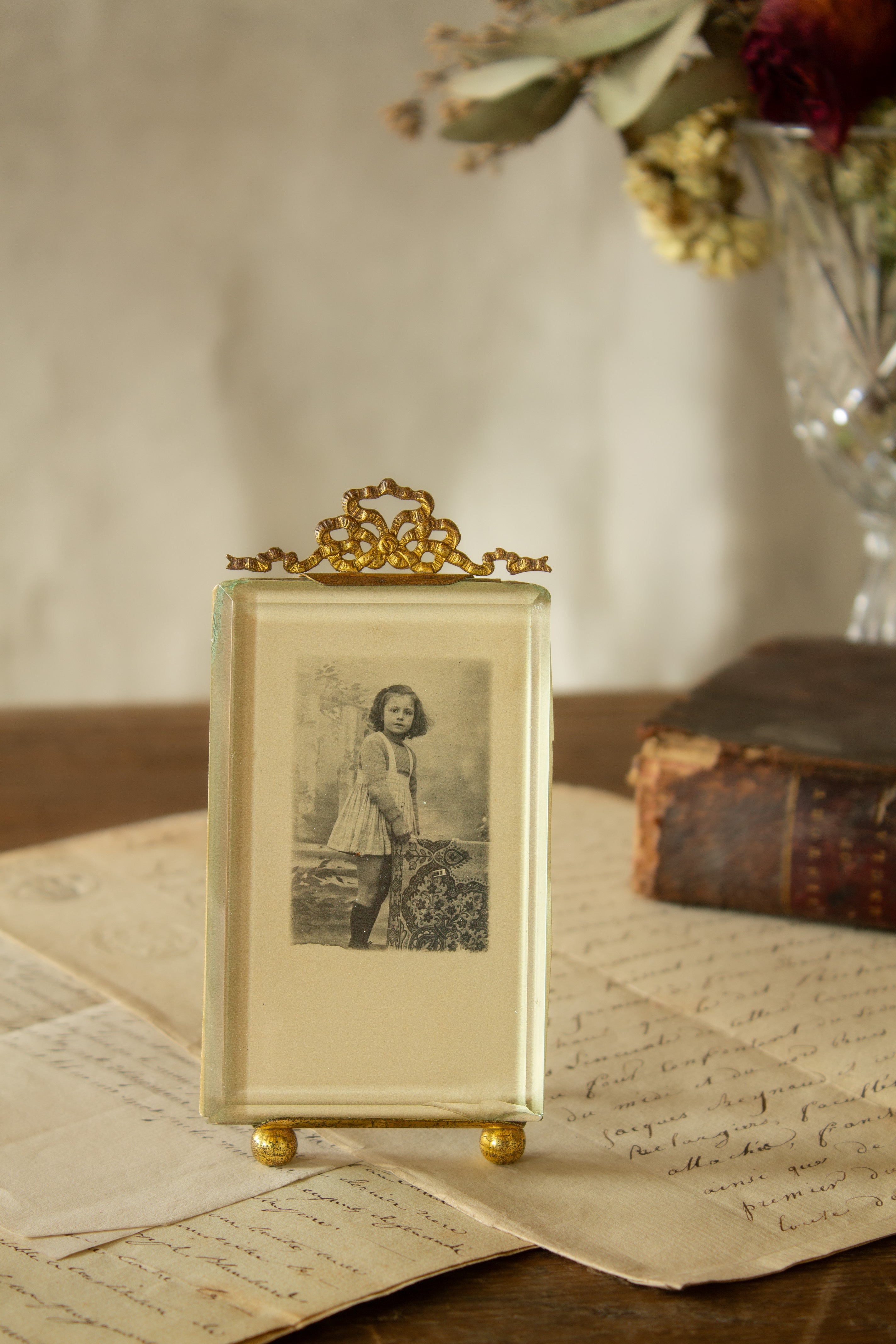 Antique French gilt metal bow-top photo frame sourced in Paris, with ball feet, thick glass, antique photograph of a young girl in a pinafore and knee-high socks, and French photographer’s card with beautiful script lettering on the back.