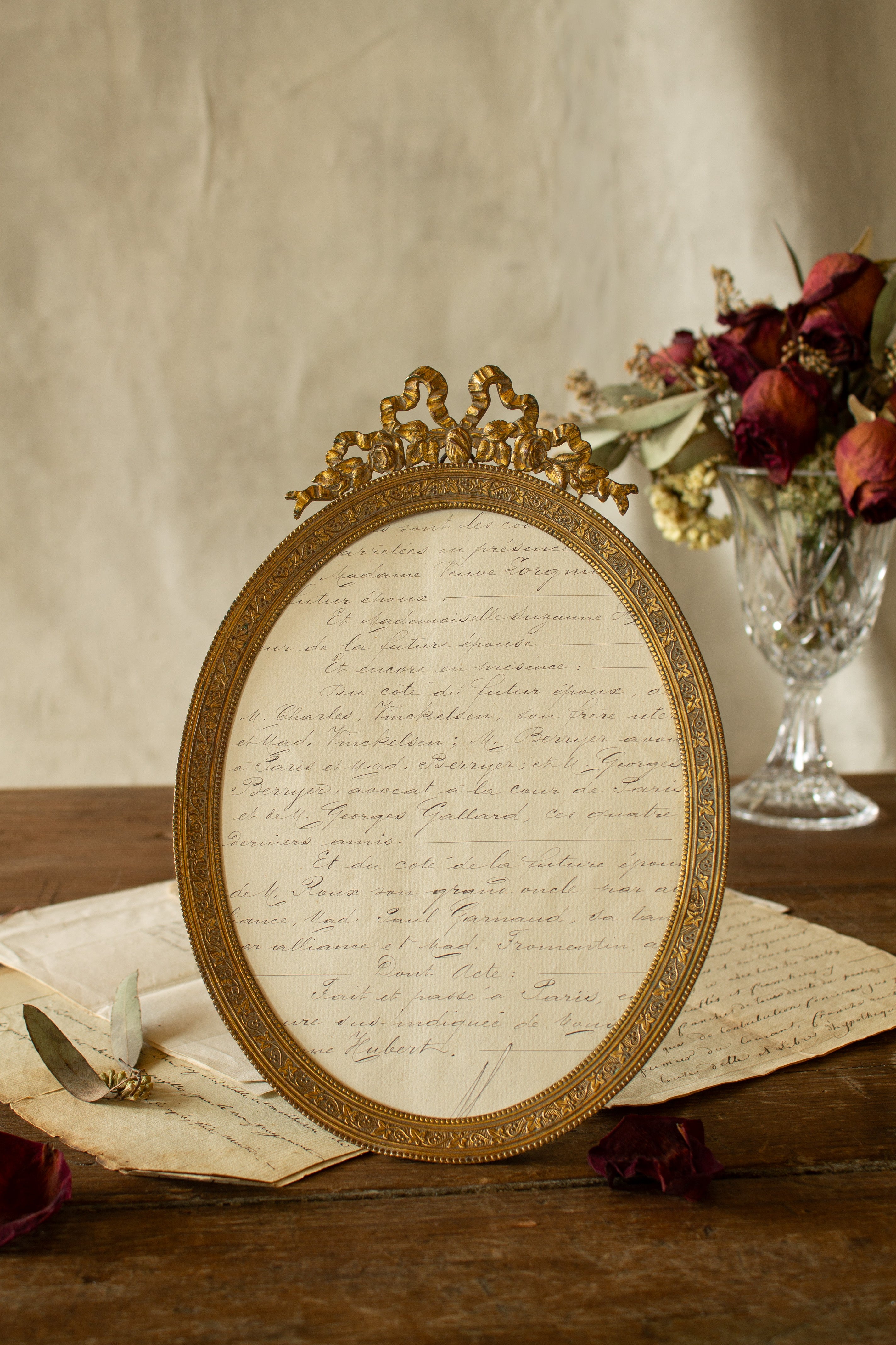 Large antique French gilt metal oval frame sourced in Paris, with bow crest, tiny roses, ivy detail, double beaded border, easel back, hanging loop, and antique French document paper inside.