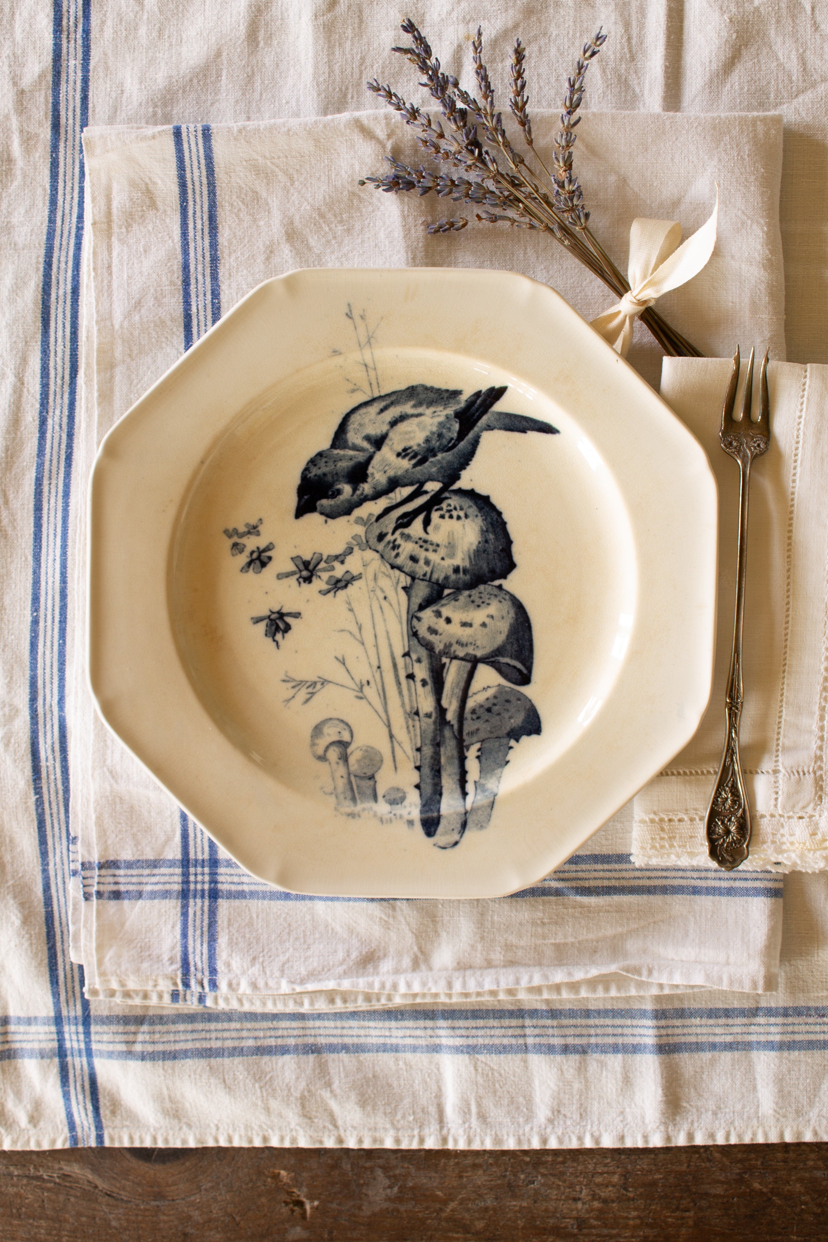 Antique Canova transferware plate with dark blue bird and mushroom motif on cream earthenware, styled on blue-striped linens.