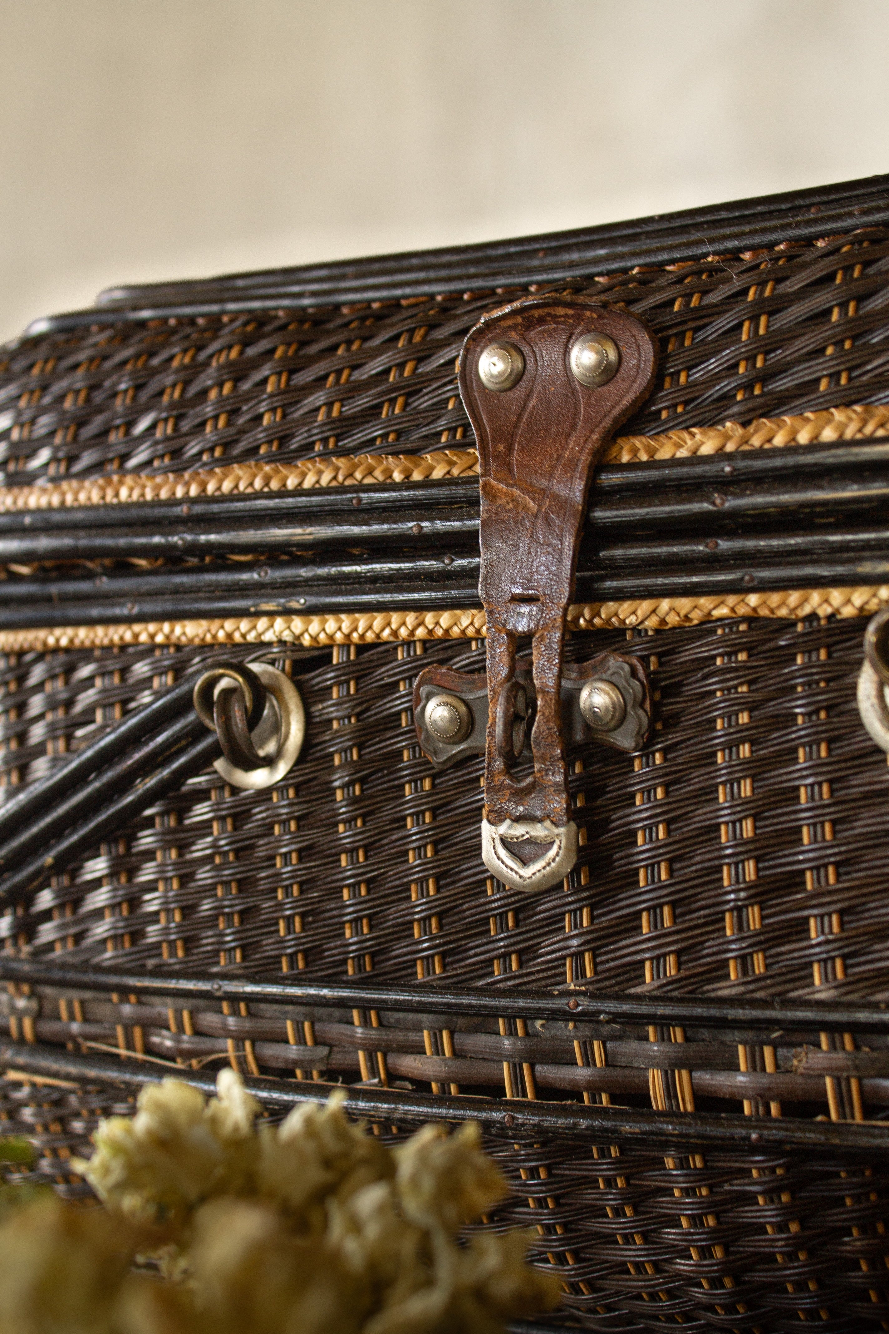 Close view of the worn leather latch and metal hardware on an antique wicker fishing creel basket.