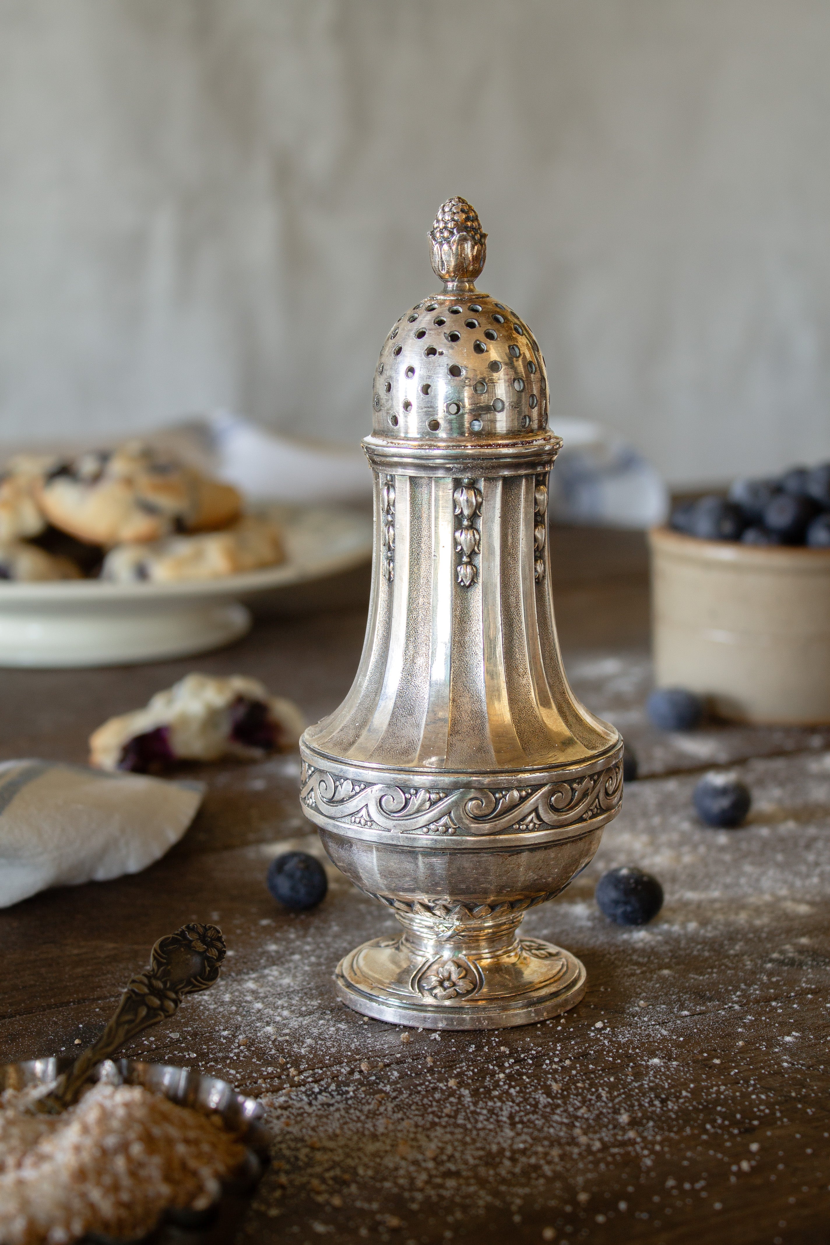 French Gallia silver-plated sugar caster with pierced dome lid, floral finial, fluted body, and ornate scrollwork.