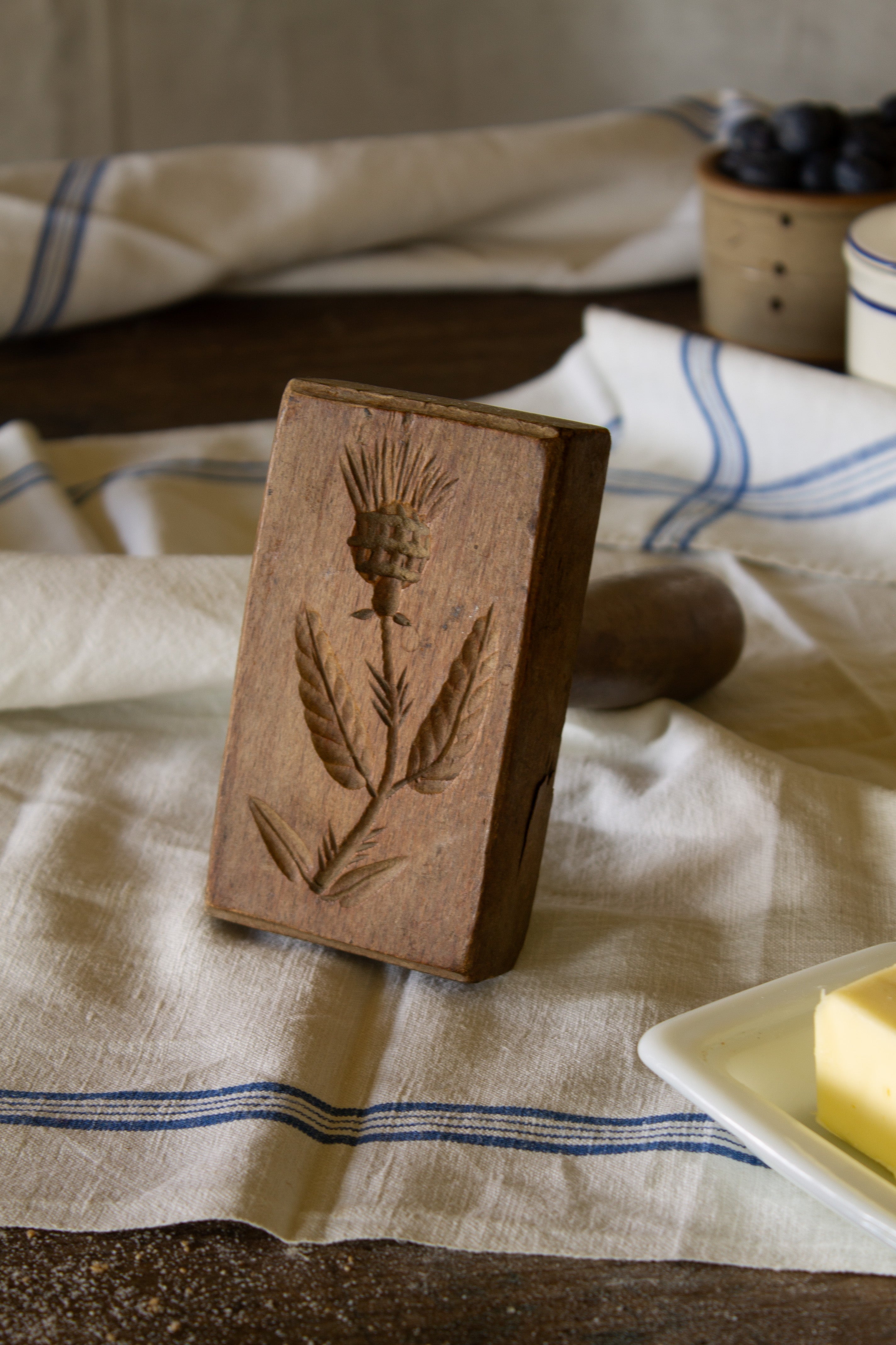 Antique French wooden butter stamp with carved thistle design, beveled stamp face, and turned wooden handle.