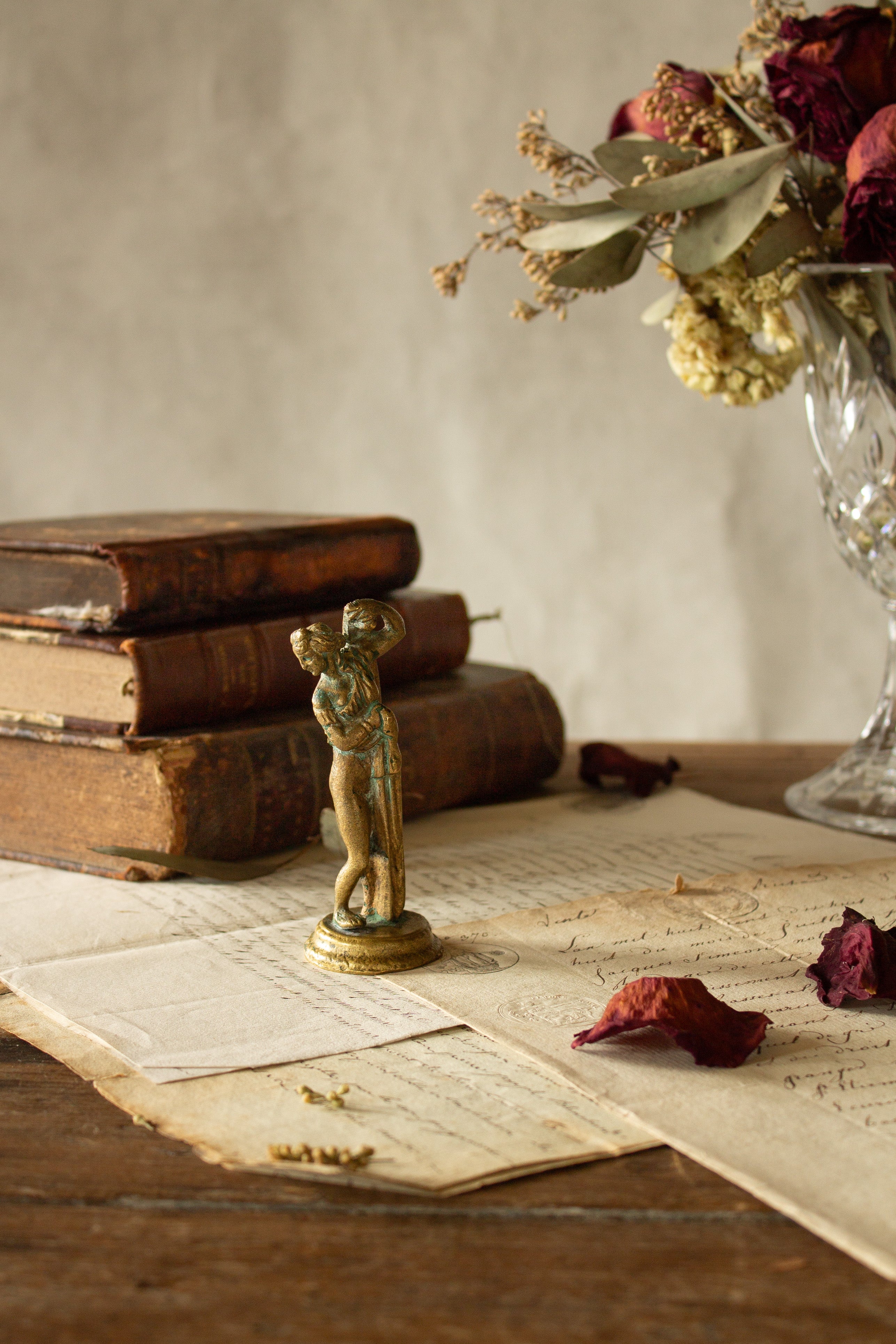Small antique French bronze-alloy figural statuette sourced in Paris, showing a playful female figure lifting her dress and glancing back, with aged gilt finish, verdigris, and round base.