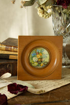 Small French hand-painted miniature floral still life in a turned wood frame with gilt copper-alloy bezel, glass front, roses, blue flowers, yellow blooms, greenery, and tiny blue eggs.