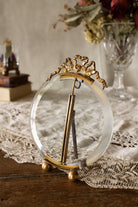 Small antique French round gilt metal photo frame with bow crest, beveled glass, ball feet, easel back, and hanging loop, sourced in Paris.