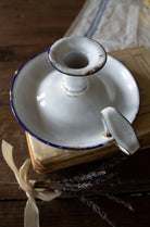 Antique French white enamelware chamberstick candle holder with cobalt blue rim, handle, and rustic chippy patina.