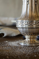 Detail of the raised scrollwork band and fluted body on a French Gallia silver-plated sugar caster.