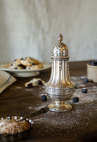 French Gallia silver-plated sugar caster styled on a wooden table with pastries, blueberries, and powdered sugar.