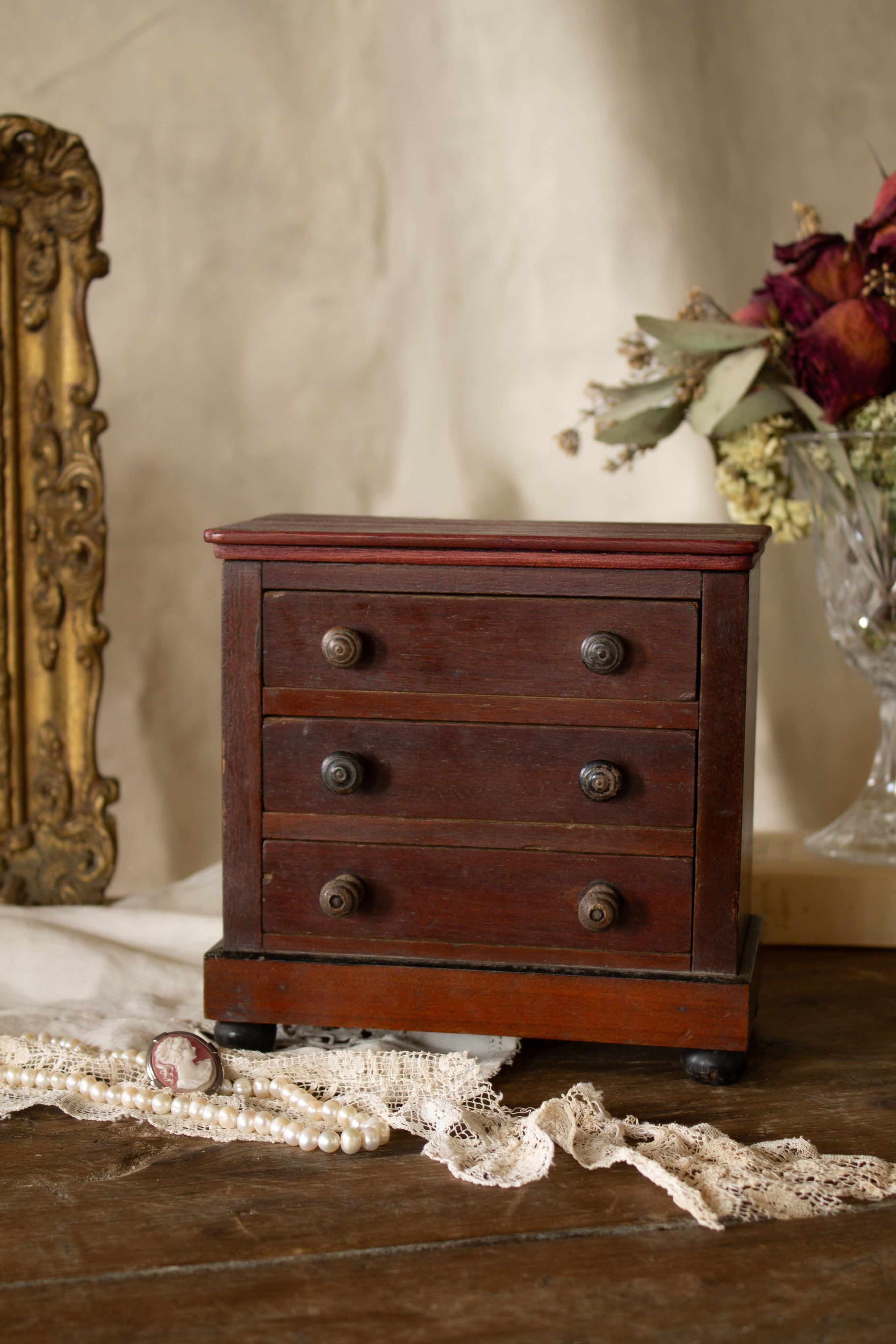 Antique French miniature veneered tabletop chest of drawers with three working drawers, warm reddish brown wood, turned knobs, bun feet, and paper label fragment