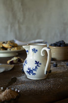 Antique French Saint-Uze style creamer with cobalt-blue floral decoration, curved handle, and creamy glazed ceramic body.