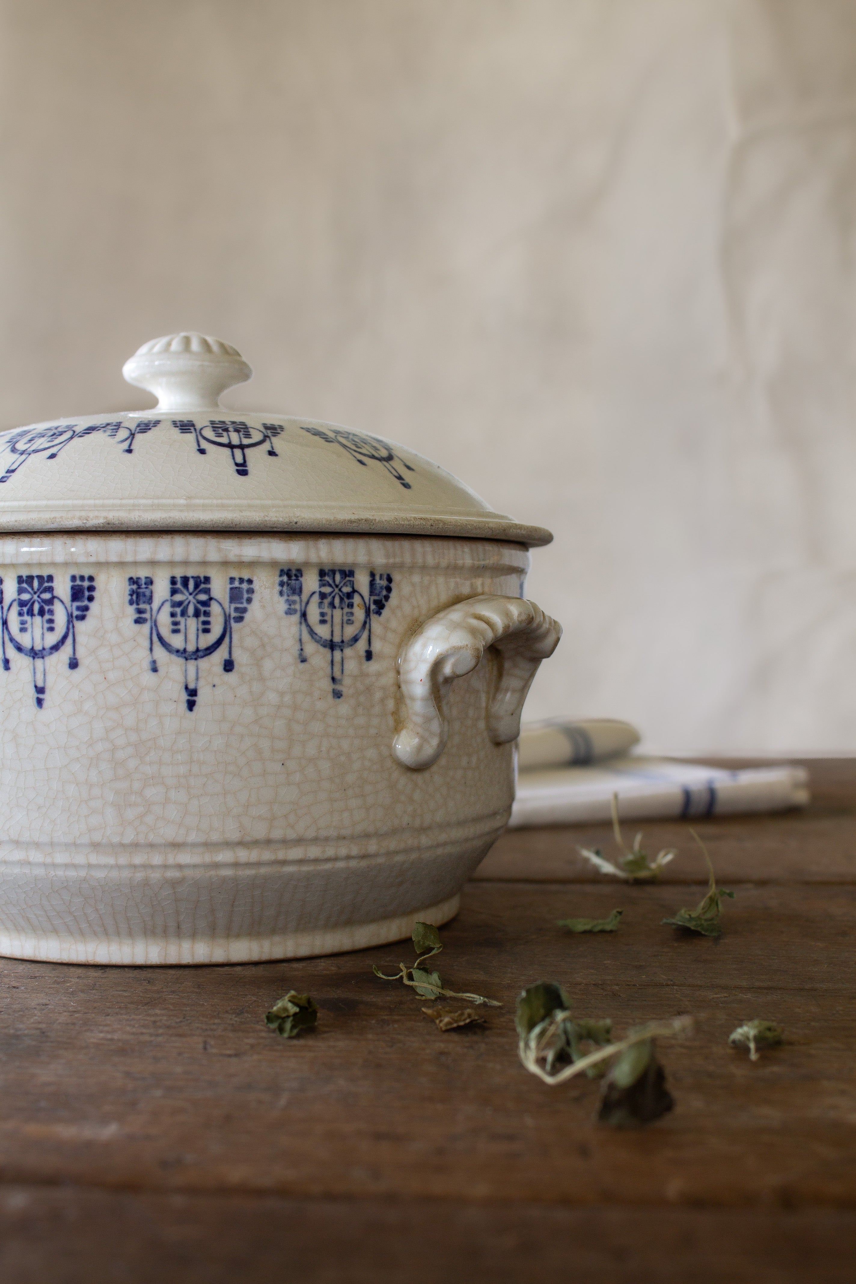 Antique French Saint-Uze style blue and white lidded tureen with cobalt stamped pattern, crackled cream glaze, worn handles, and flower-form finial.