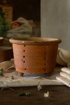 Antique French terracotta three-footed faisselle cheese mold with hand-pierced drainage holes and warm aged earthenware surface.