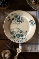 Antique French Terre de Feu de Grigny plate with aged blue-green botanical floral sprays on a warm cream ground.