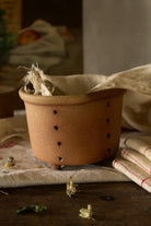 Antique French three-footed faisselle with perforated sides, irregular handmade form, and softly aged earthenware surface.
