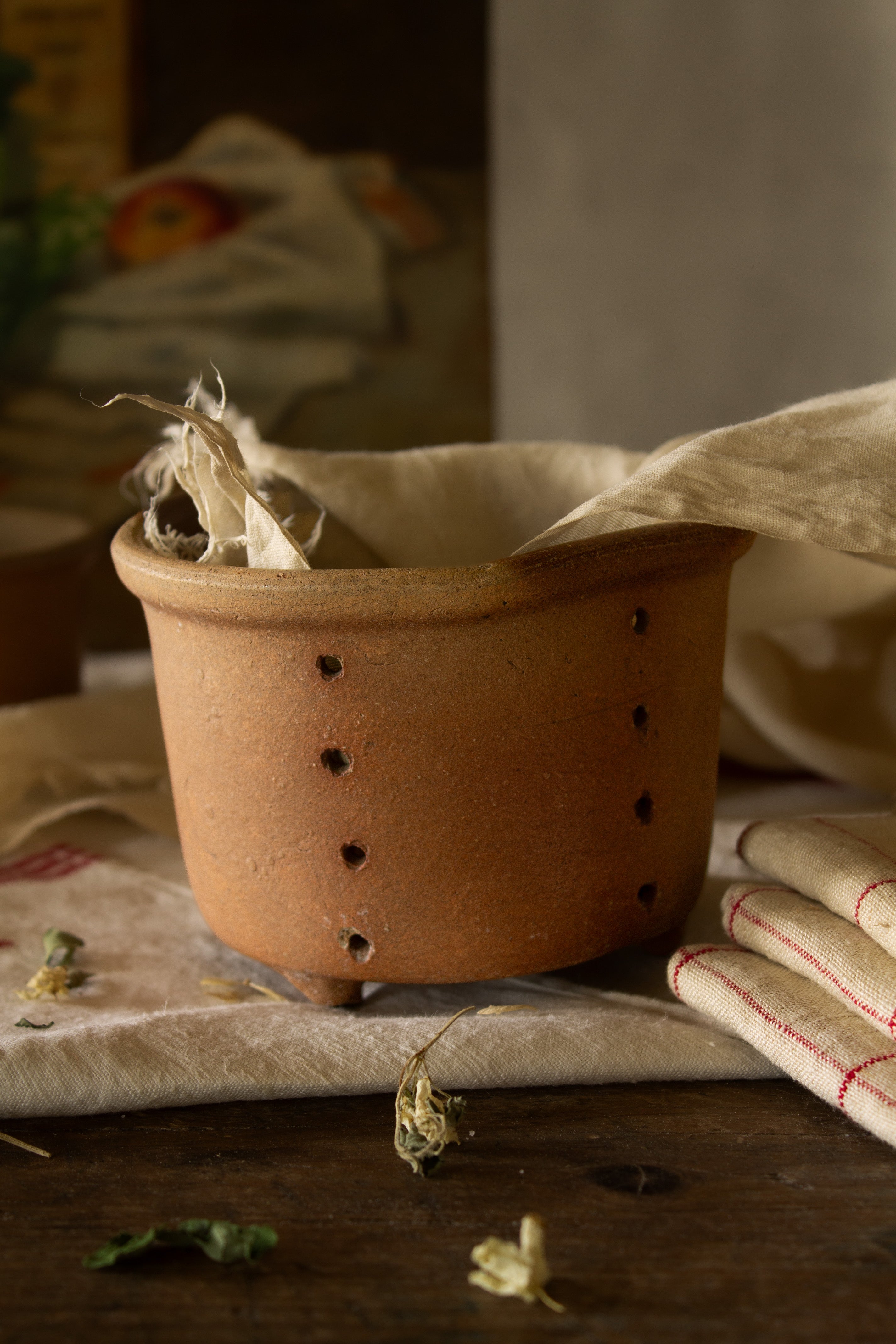 Antique French three-footed faisselle with perforated sides, irregular handmade form, and softly aged earthenware surface.