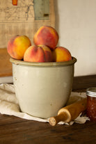 Large antique cream stoneware preserve crock with dark interior glaze, styled with fresh peaches and an antique wooden rolling pin.