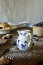 Miniature antique French Saint-Uze style creamer with cobalt-blue floral decoration, curved handle, and creamy glazed ceramic body.