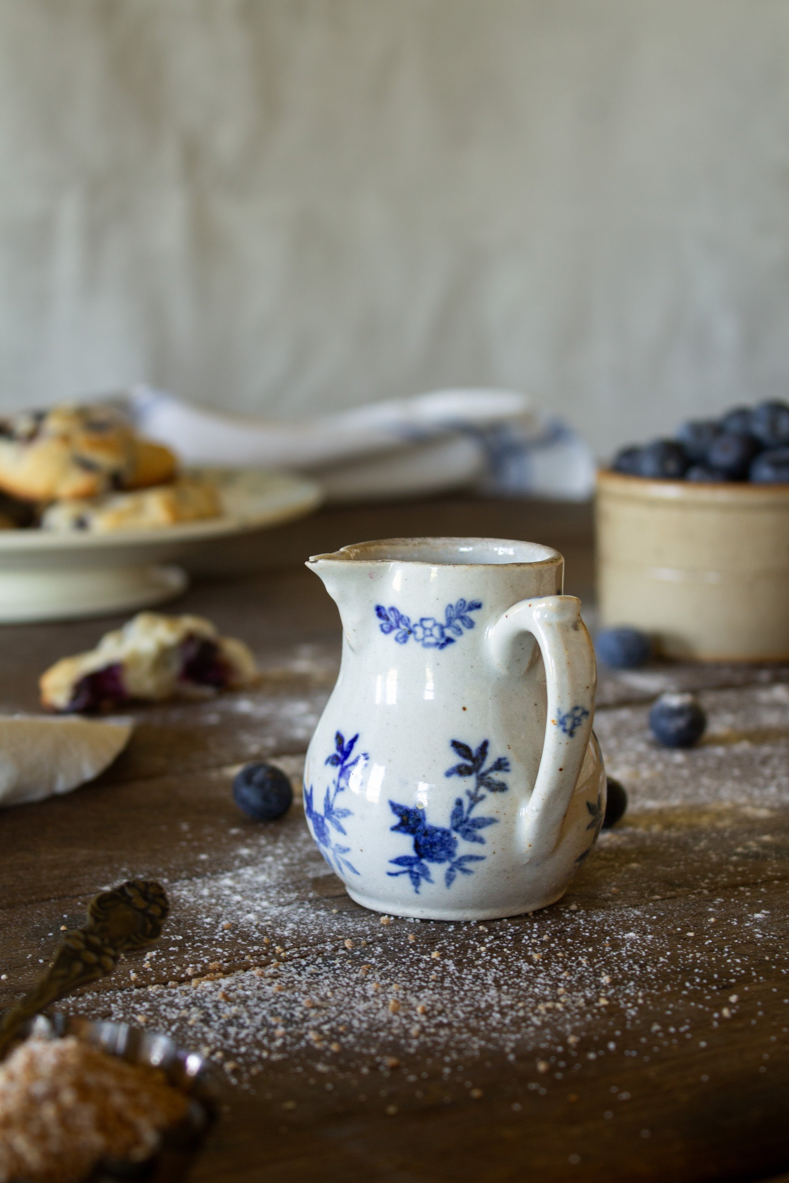 Miniature antique French Saint-Uze style creamer with cobalt-blue floral decoration, curved handle, and creamy glazed ceramic body.