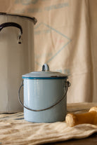 Small French blue enamelware lidded canister with wire handle, worn rim, rust spots, and pale blue enamel surface.