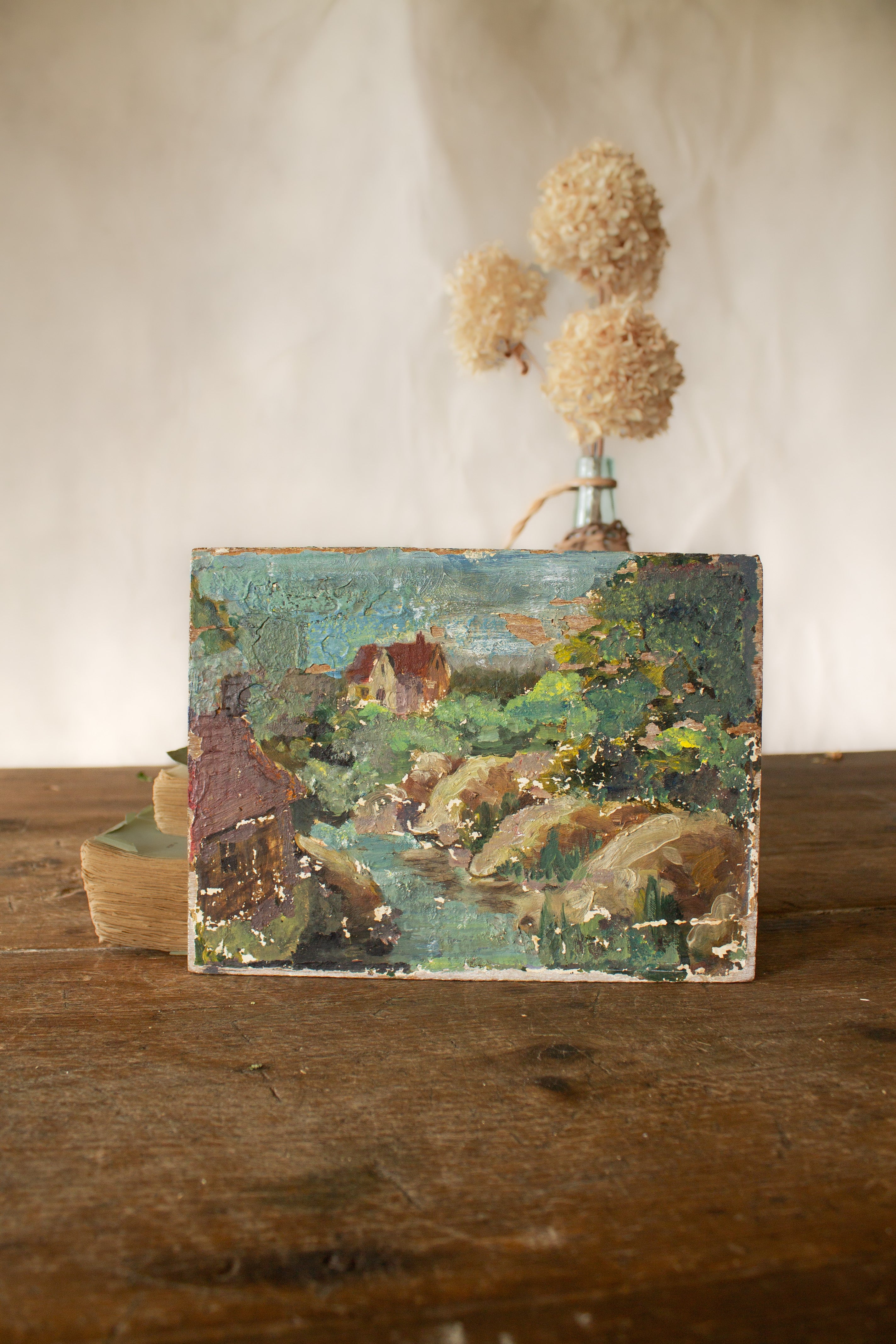 Small vintage French landscape painting on board with rustic chippy surface and earthy blue-green tones.