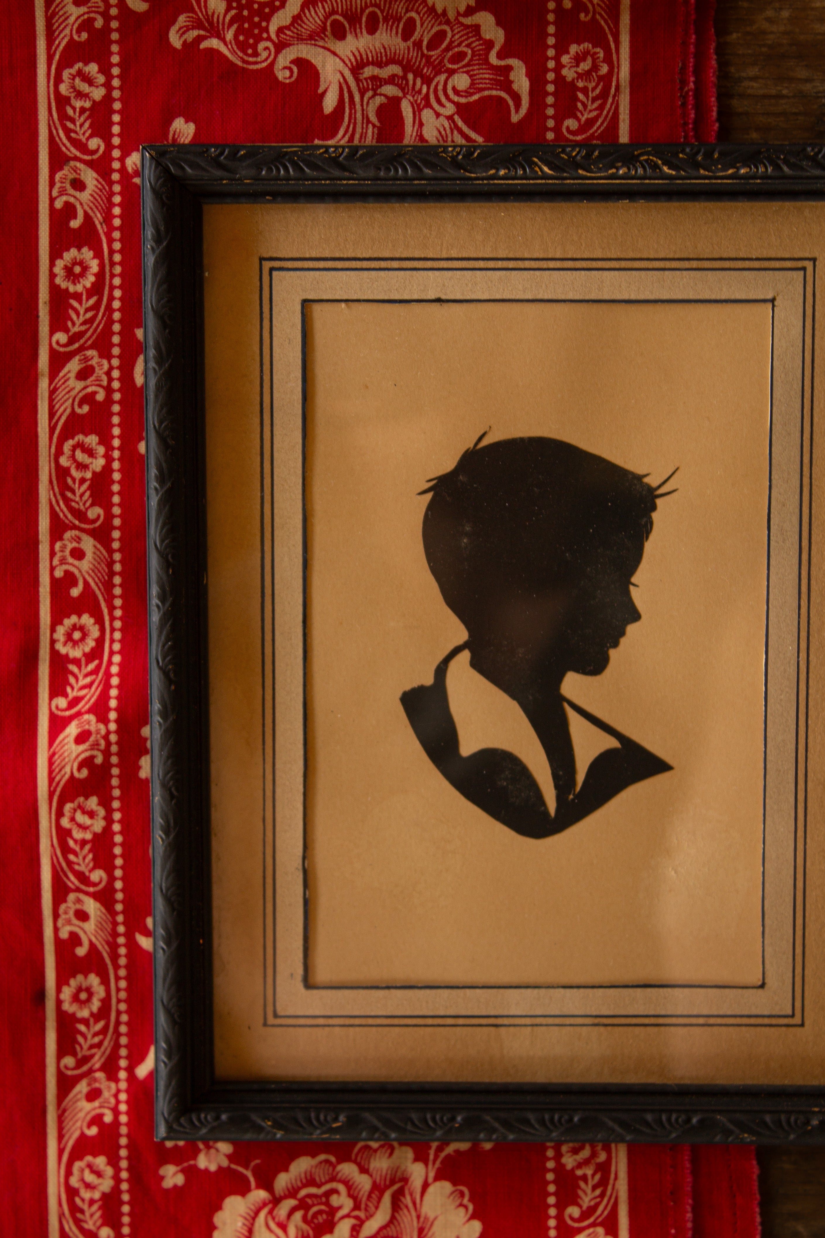 Vintage framed boy silhouette portrait with hand-cut mat, pen-and-ink border, painted black frame, and warm aged paper tones.