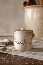 Small ceramic jar labeled 'Basilic' on a rustic surface with a blurred background
