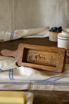 Vintage French wooden butter mold with long handle, cow and fence design, worn varnished finish, and visible wood grain.