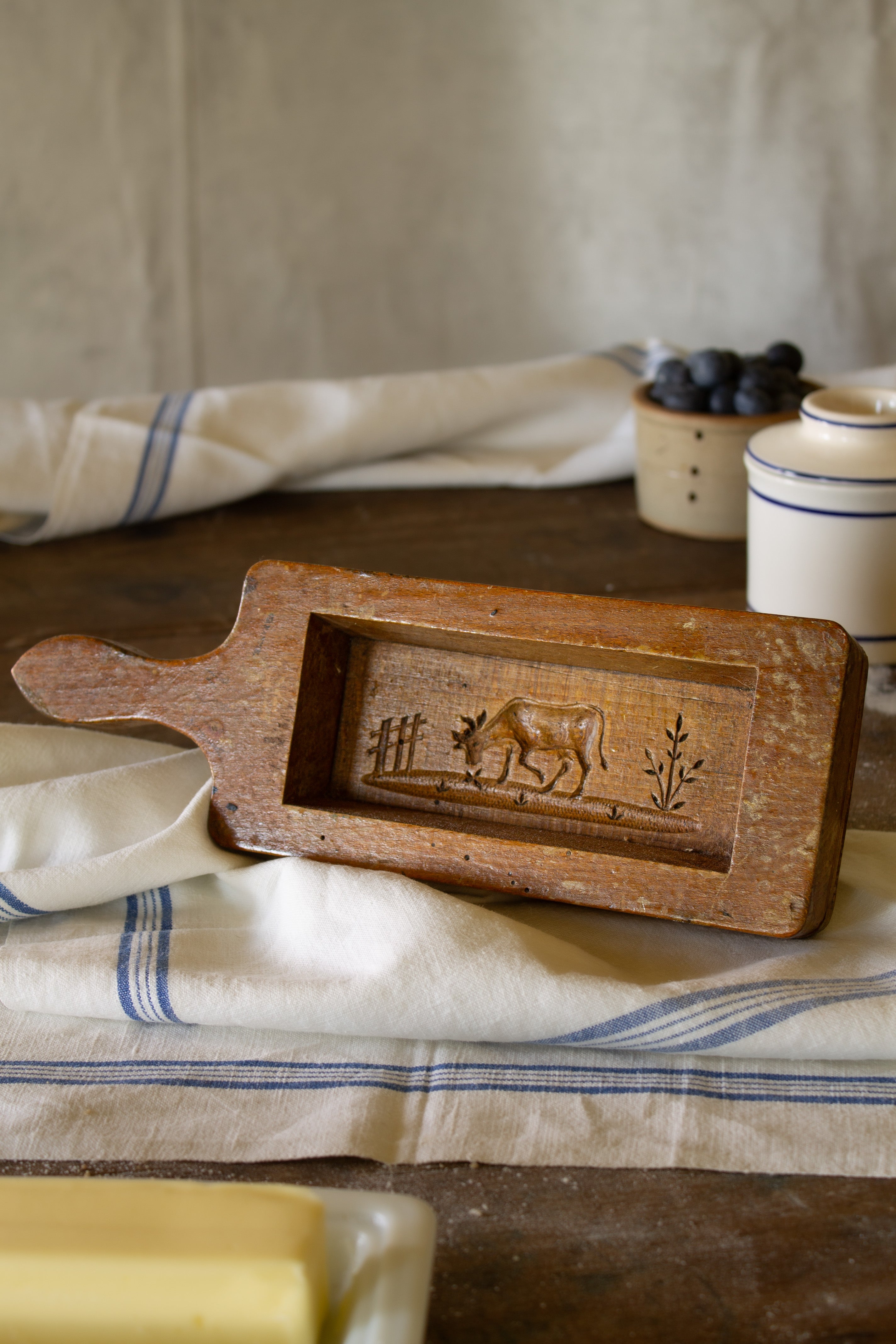 Vintage French wooden butter mold with long handle, cow and fence design, worn varnished finish, and visible wood grain.