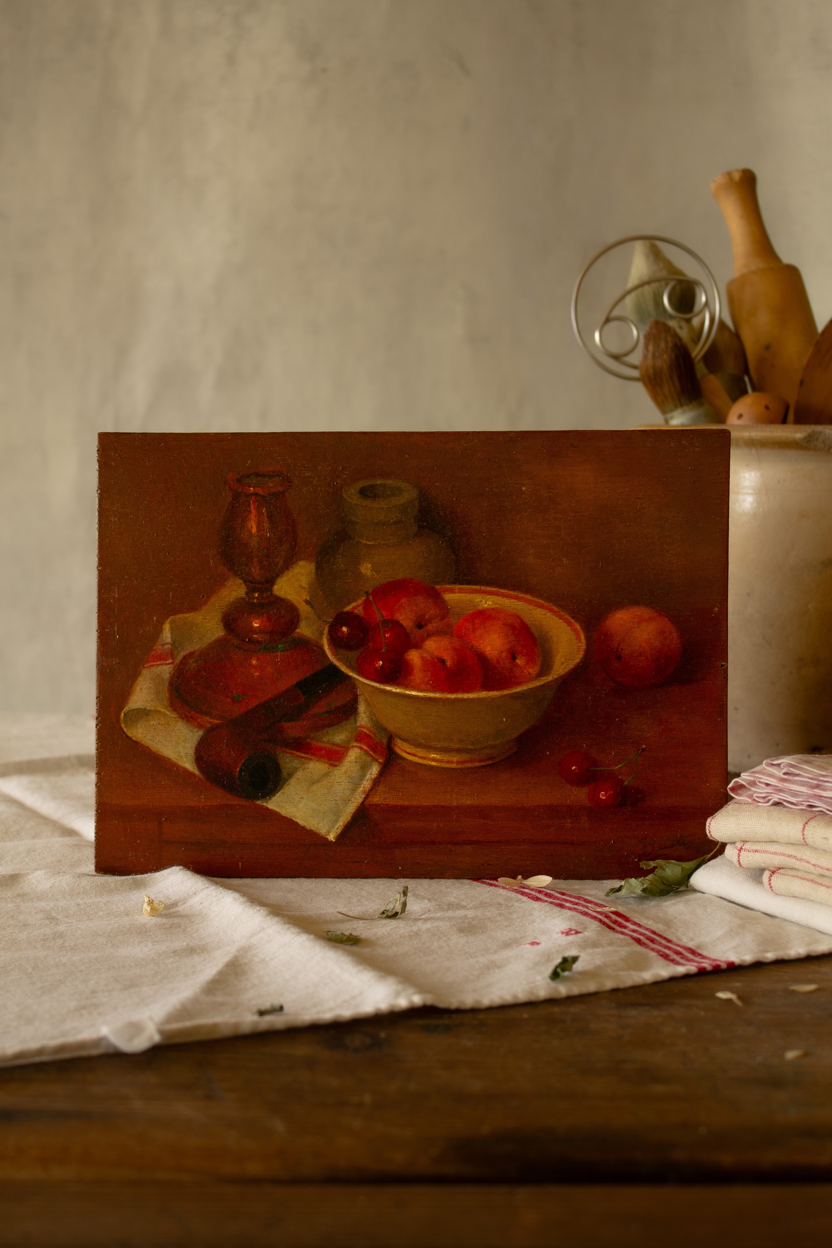 Vintage French moody still life painting on wood panel with peaches, cherries, pottery, copper candlestick, and red-striped kitchen cloth.