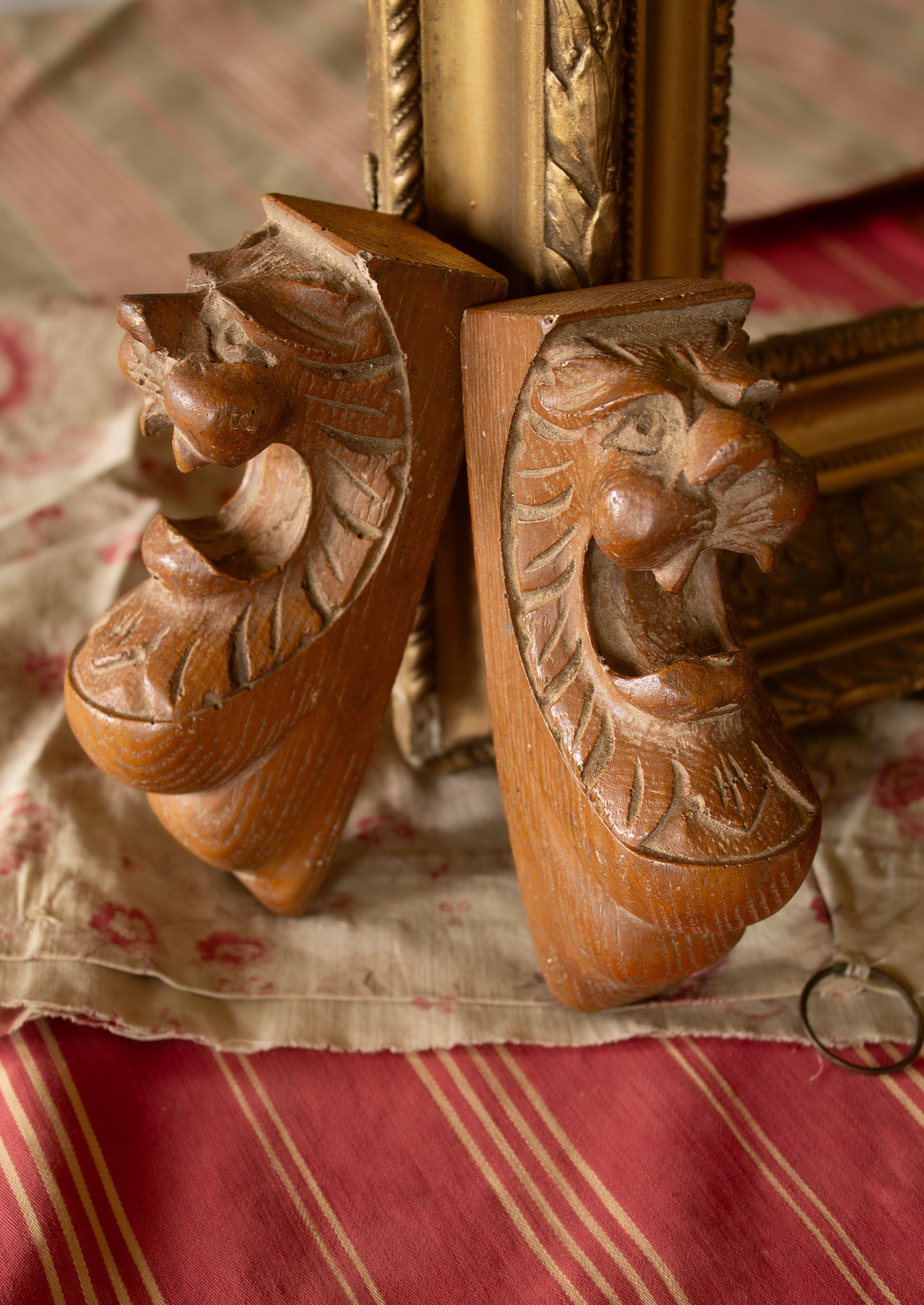 Pair of vintage molded plaster lion-head corbels with warm brown faux-bois finish, shown from the front.