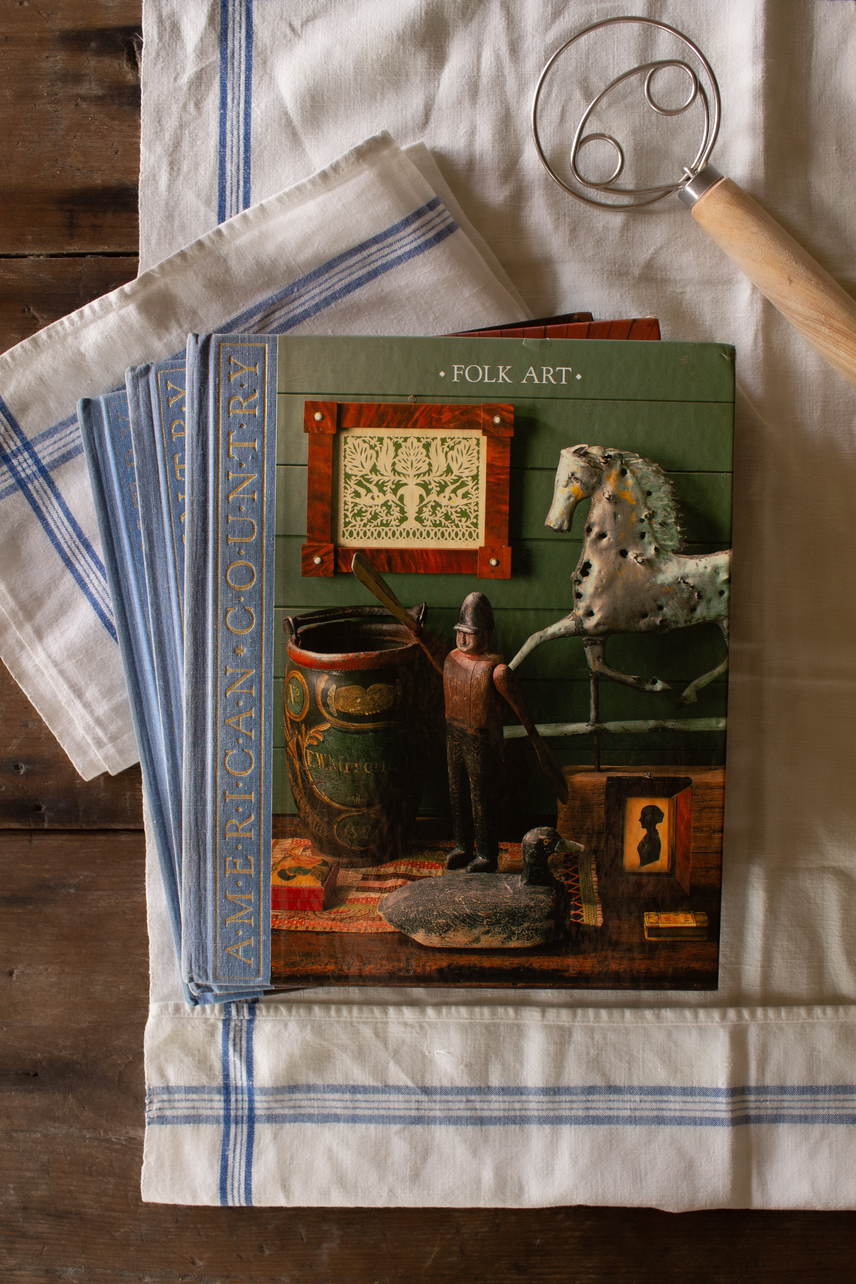 Vintage set of three Time-Life American Country books including Folk Art, The Country Home, and Country Furniture styled on blue and white linen, featuring primitive country, Americana, folk art, pottery, early American furniture, and country interior design reference.